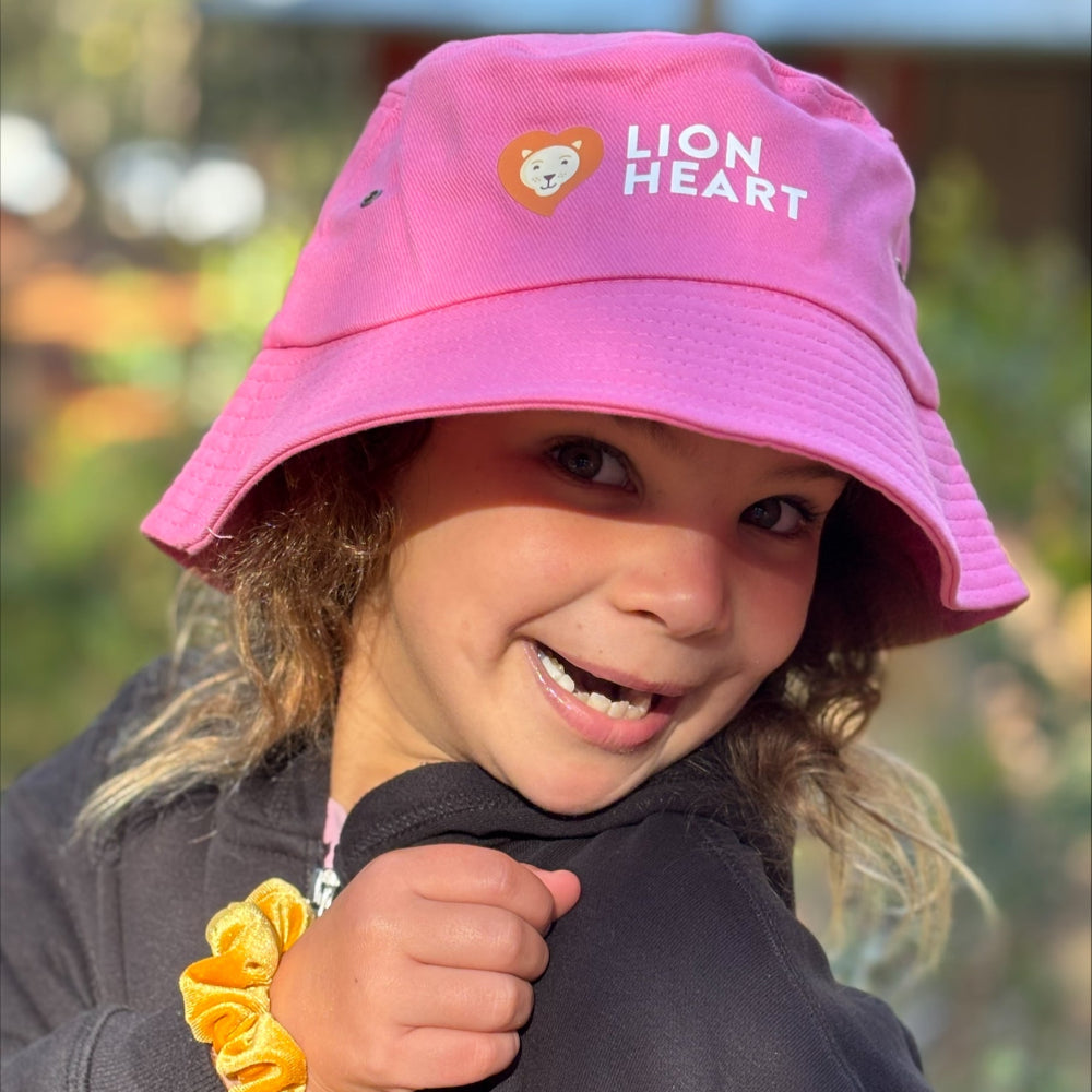 Child wearing a pink 'Lion Heart' hat with a blurred outdoor background