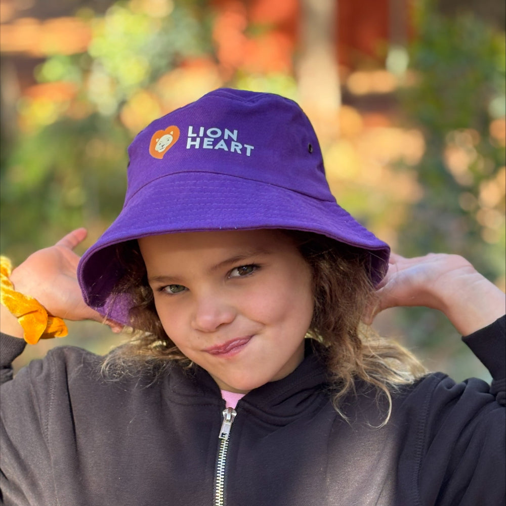 Child wearing a purple 'Lion Heart' bucket hat with a blurred natural background